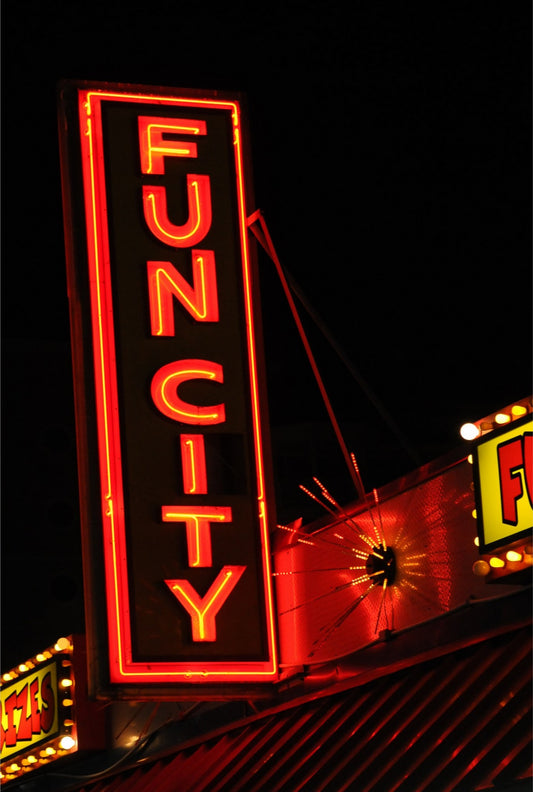 A vertical neon sign reading 'FUNCITY' in glowing red letters on a black background, photographed at night above a building with other illuminated signs partially visible.