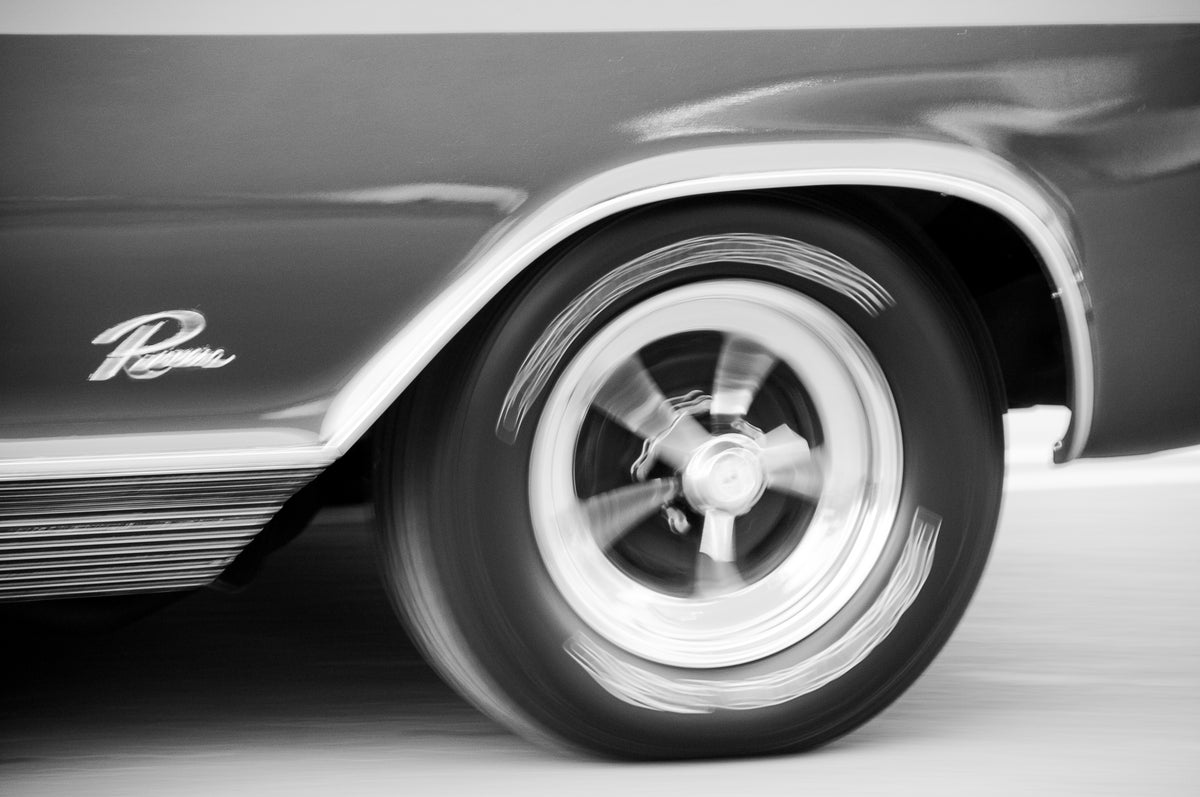 Black and white close-up photograph of a classic car wheel and fender with a visible 'Rough' script emblem on the side.